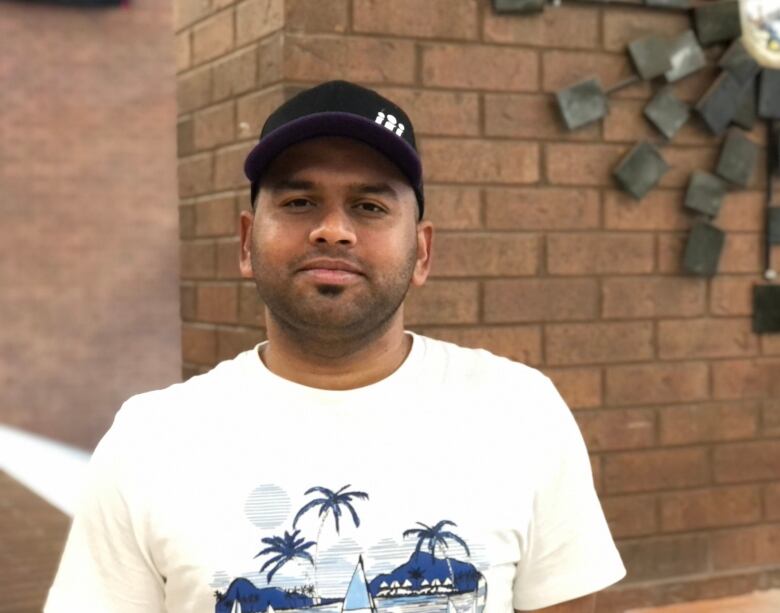 Man wearing black ball cap and white shirt.