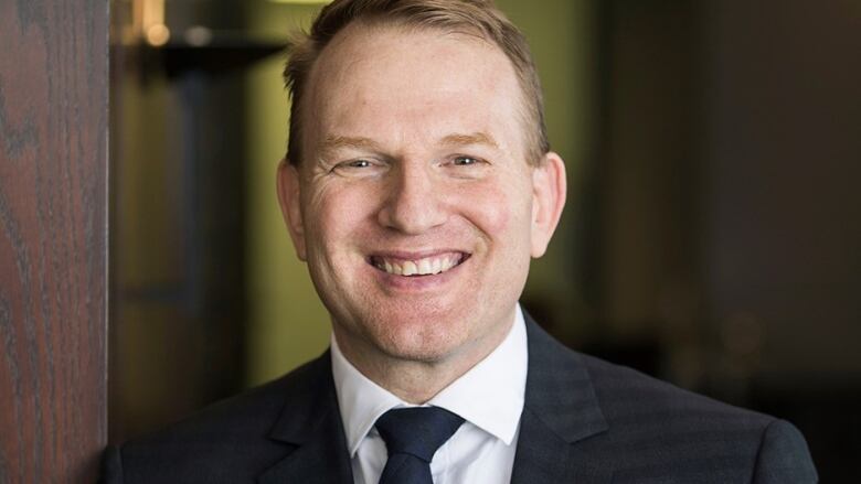 Medium shot of smiling individual with blond hair wearing a blue tie. 