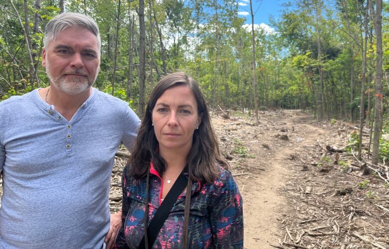 A man and a woman stand on a wooded trail.