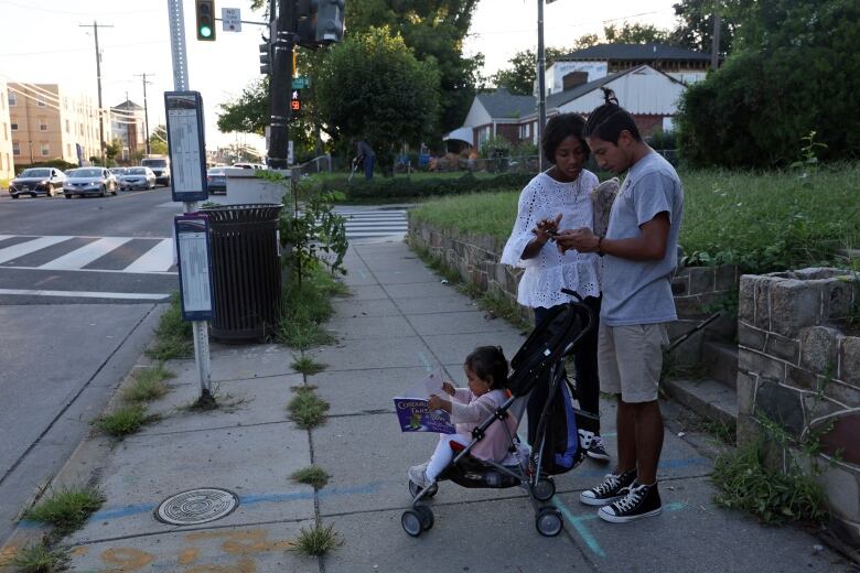 A couple are seen looking a map on a city sidewalk, beside their daughter in a baby stroller.