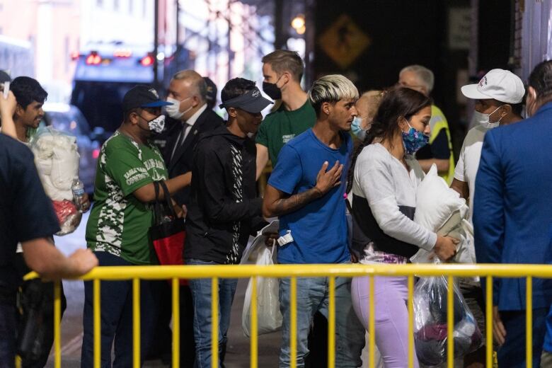 A group of people, some with masks, are shown outside at a bus terminal.