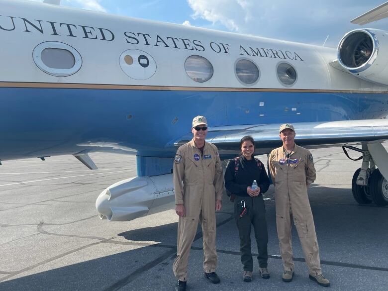 Two men in military uniform pose with young woman in front of large plane. 