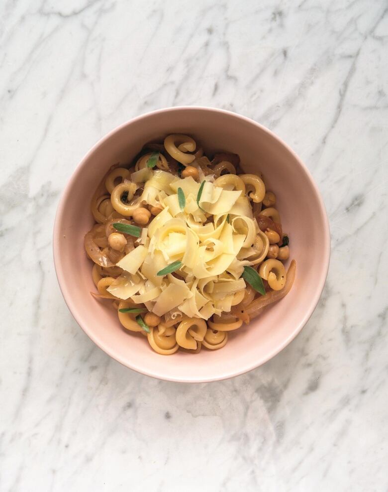 overhead shot of a bowl of short pasta topped with onions and cheese, sitting on a marble surface