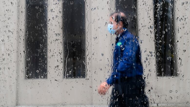 A pedestrian walks alongside businesses on a rainy day while wearing a protective mask during the COVID-19 pandemic