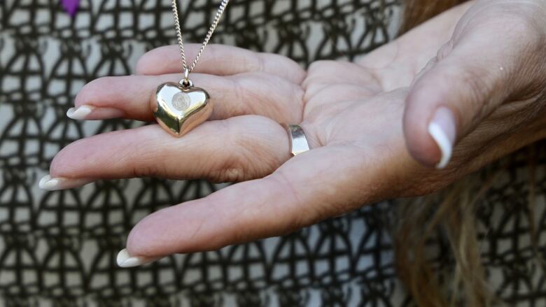 A mother's left hand hold a golden, heart-shaped locket containing some of the ashes of her son who died of a toxic drug overdose when he was 25 years old.