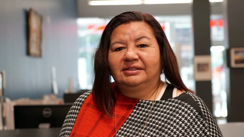 A woman with a red and black shawl poses for a photo in an office.