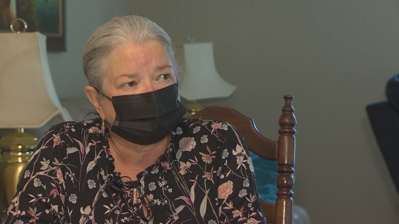 A woman in a mask sits at her kitchen table during an interview.