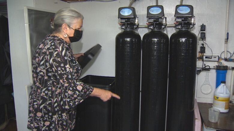 A woman opens the lid of a salt storage bin next to three large black tanks.