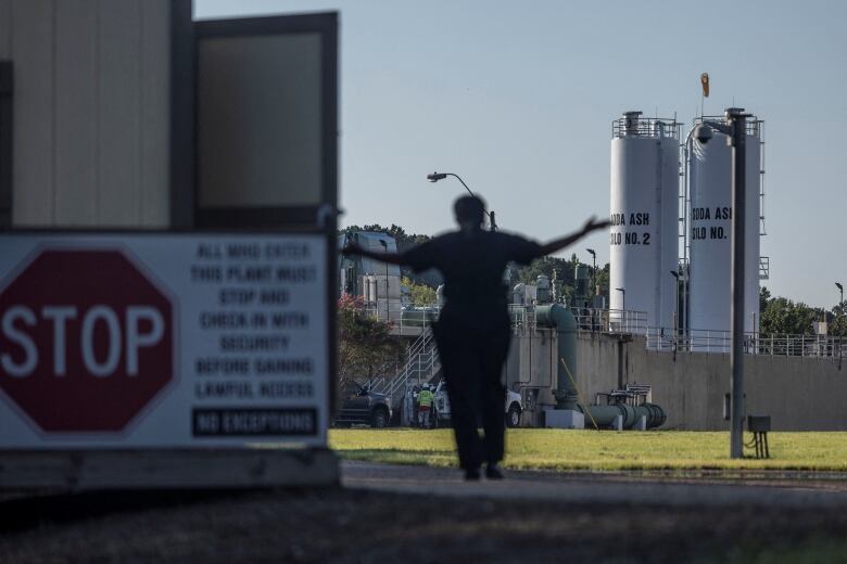 A silhouette of a person holding their arms up in what appears to be a big shrug next to a large stop sign and in front of two water towers. 