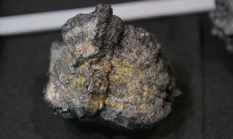 A lump of mineral with gold flecks sits on a black table