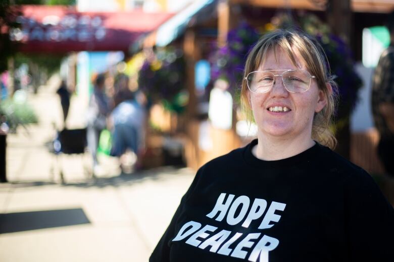 A woman wearing a black shirt that says hope dealer and aviator glasses smiles for the camera.