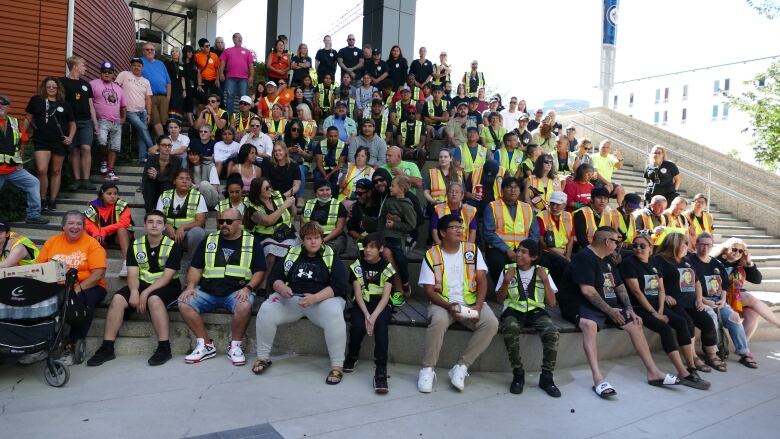 A large group of people sit on the steps of a building for a group photo.