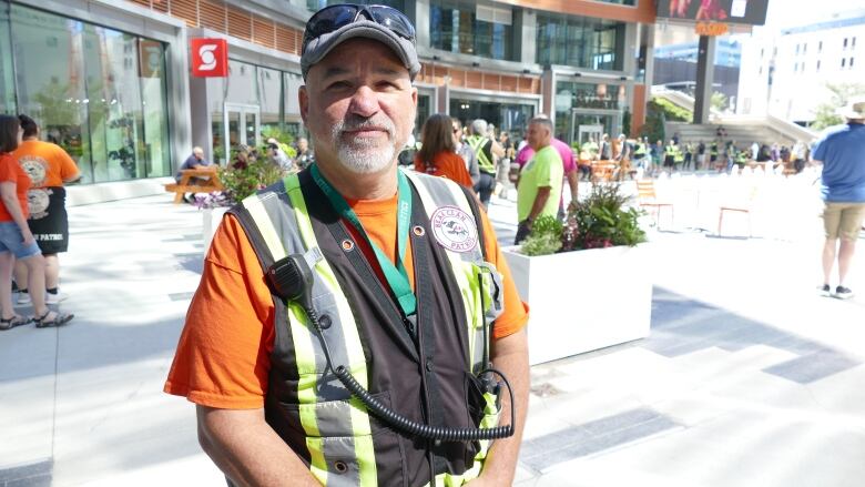 A portrait of a man in a vest and an orange shirt standing on a city sidewalk.