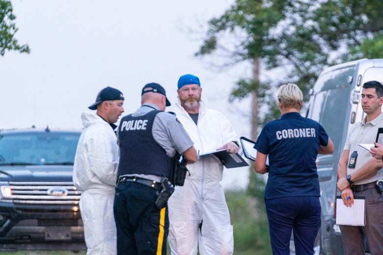 Police officers and coroners stand in a circle in an open area.