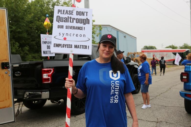 A woman wearing a hat and a blue t-shirt holding a sign requesting money from the federal government