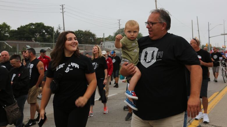 A father and daughter wearing black t-shirts, with the man holding the daughter's baby nephew