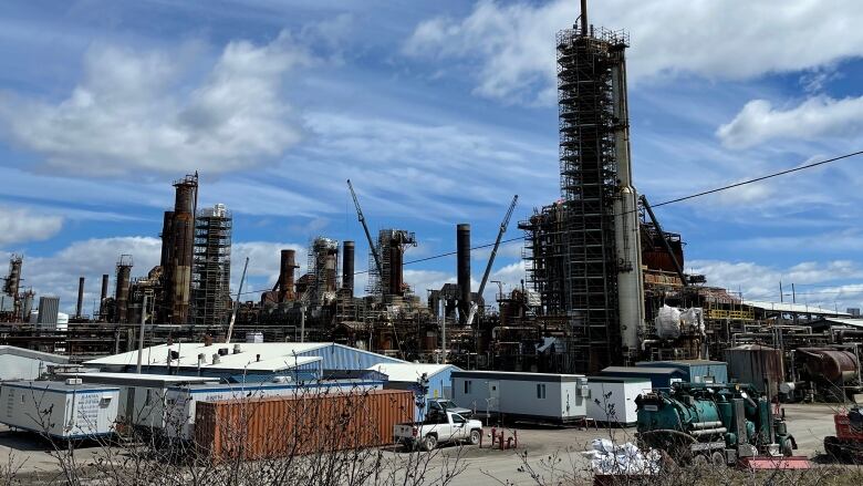 A refinery is pictured under a bright blue sky with white puffy clouds.