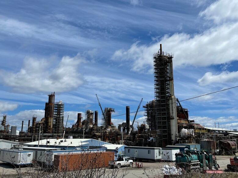 A refinery is pictured under a bright blue sky with white puffy clouds.