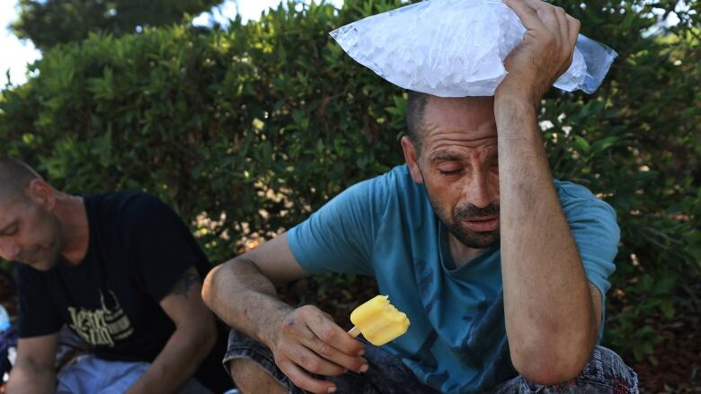 A seated man holds a bag of ice against his head.