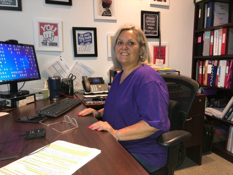 A woman wearing a purple t-shirt sitting at her desk in her office