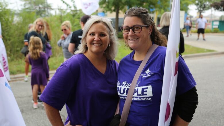 Two women wearing purple t-shirts standing beside each other and holding a flag