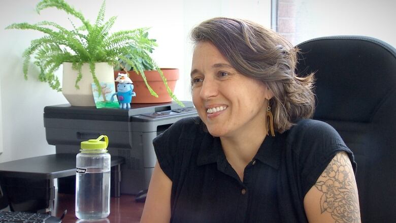 A woman sitting at a desk smiles and talks to someone else.