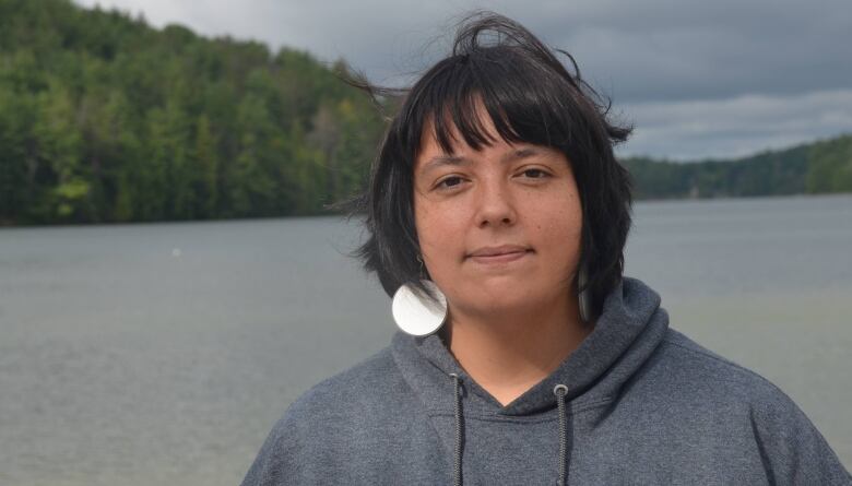 Amber Gaudreault stands in front of a lake wearing a shirt that reads 'deadly.'