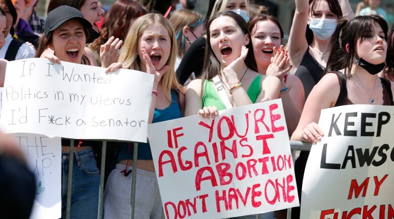 Young women holding signs and shouting behind a metal barricade.