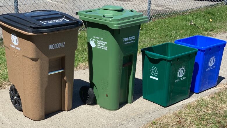 A collection of different coloured bins on the sidewalk.