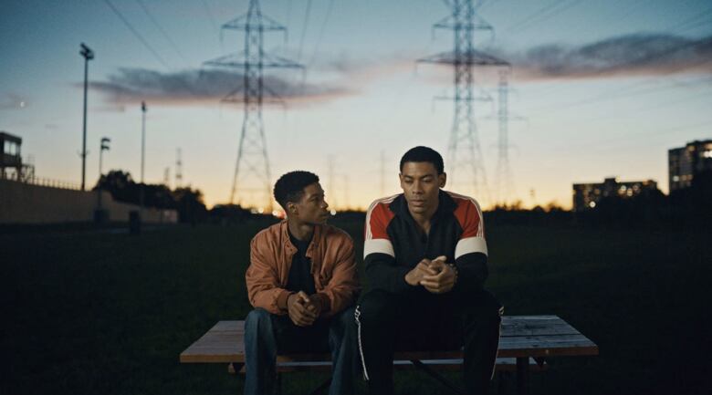 Two young Black men sit on top of a picnic table at sunset