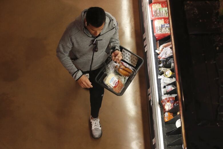 A man shops for groceries with a hand-held basket