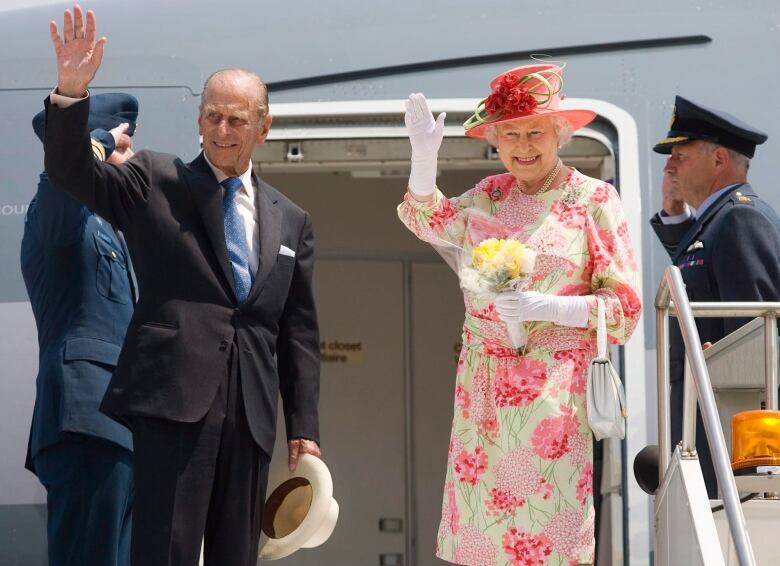 Two elderly people wave to a crowd.