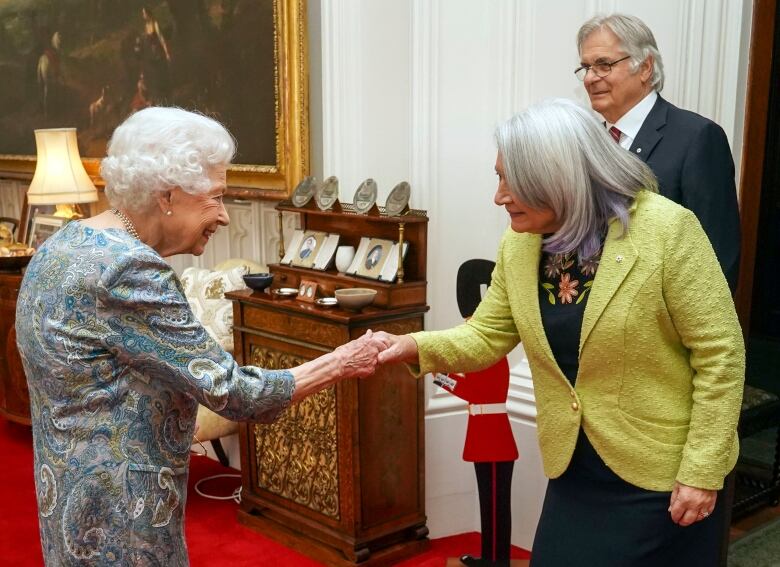 Two people shake hands as another person looks on.