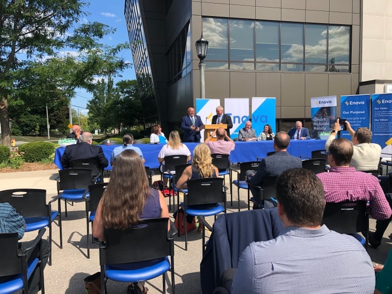 A crowd of people sit while listening to an announcement from local mayors.