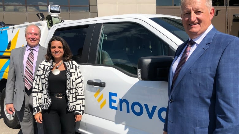 Three executives stand in front of a white pick-up truck with the logo Enova.