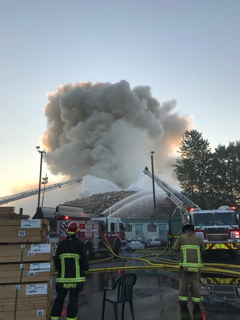 A number of firefighters pour water on a large blaze concentrated on some wood debris.