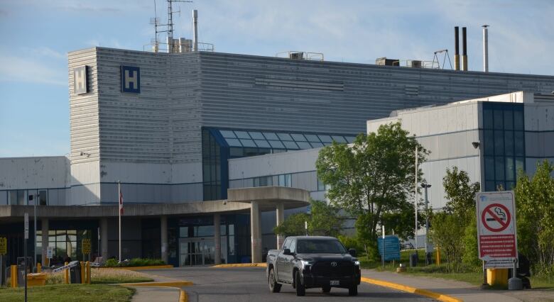 A truck drives away from a large building with an 'H' sign on the top. 