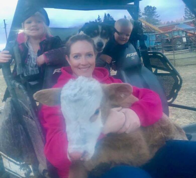 A woman hugs a cow while sitting in a tractor with two young children. 