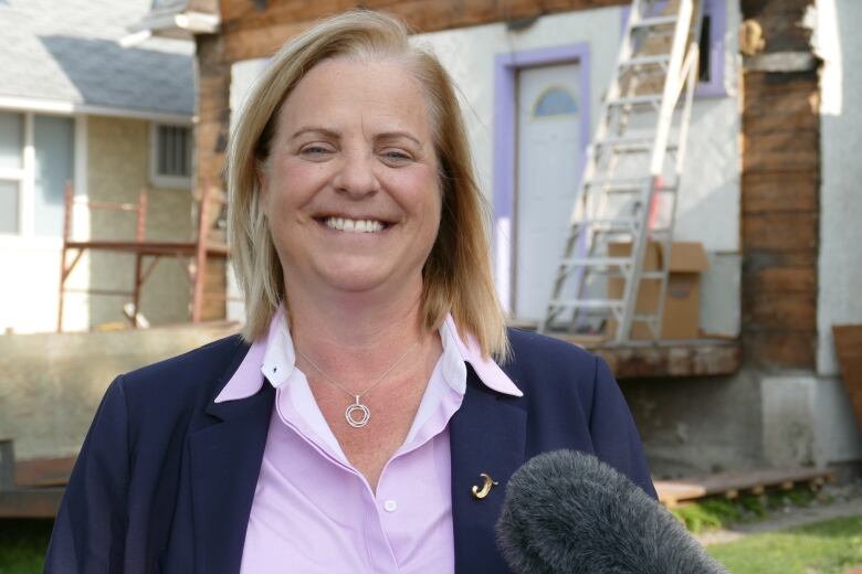 A woman is smiling, standing in front of a house that is undergoing renovations.