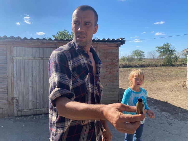 A man in a plaid shirt holds a shell casing while a young girl looks on. 