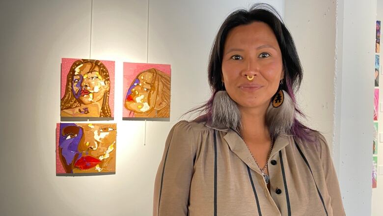 A smiling woman faces the camera in front of three paintings.