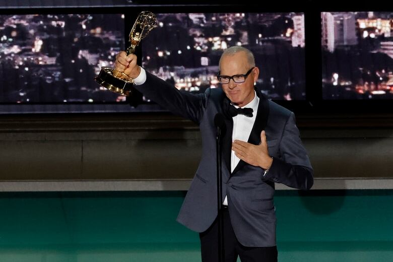 A man on stage, wearing a tuxedo, brandishes a trophy. 