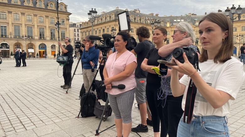 A group of people with cameras and microphones stand waiting.