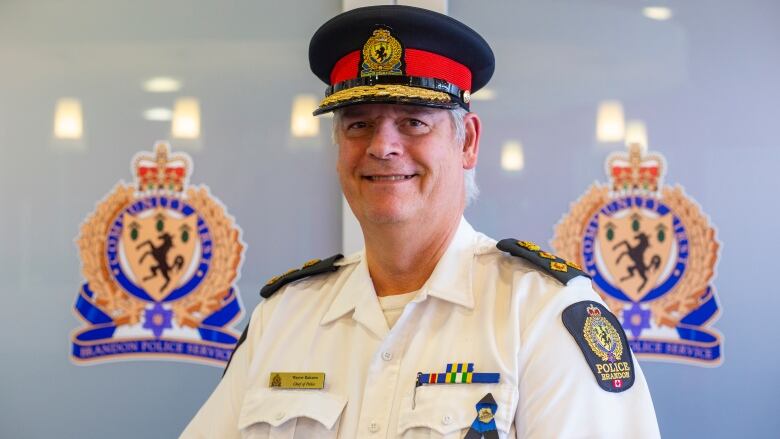 A police chief stand beside a metal teepee in front of a sign that says Brandon Police Services.