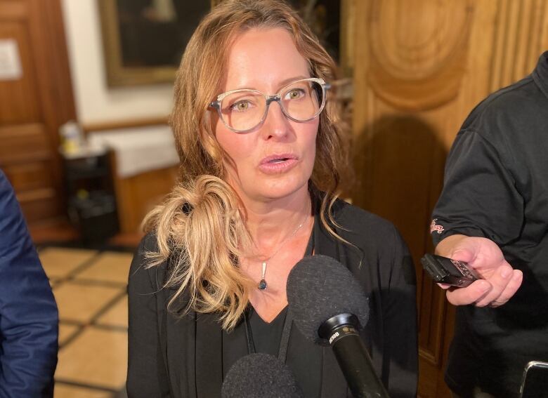 Woman surrounded by journalists speaks inti a microphone.