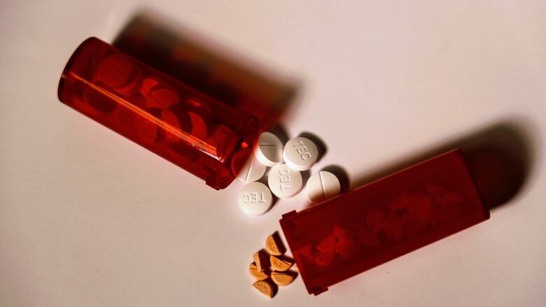 Orange pill bottles containing prescription drugs spill onto a white table.