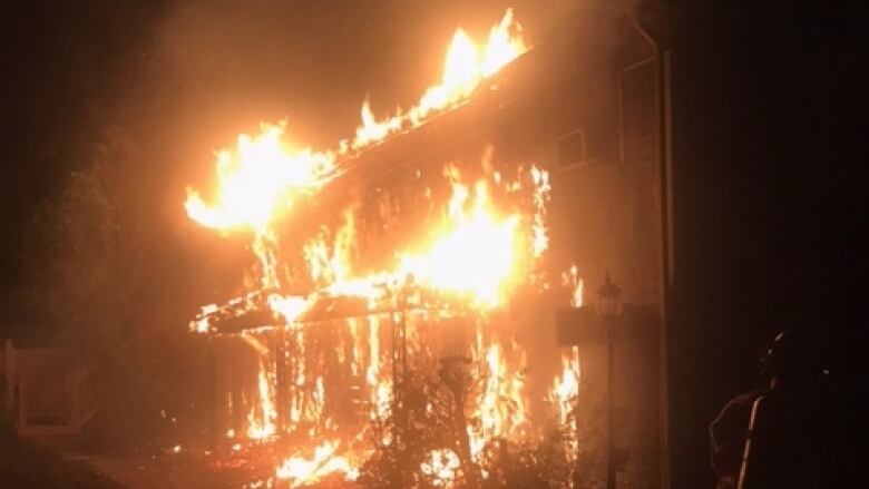 A nighttime photo shows the front of an old wooden building ablaze. 