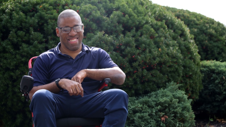 Kevin McShan sits in a wheelchair, laughing, in front of a group of bushes