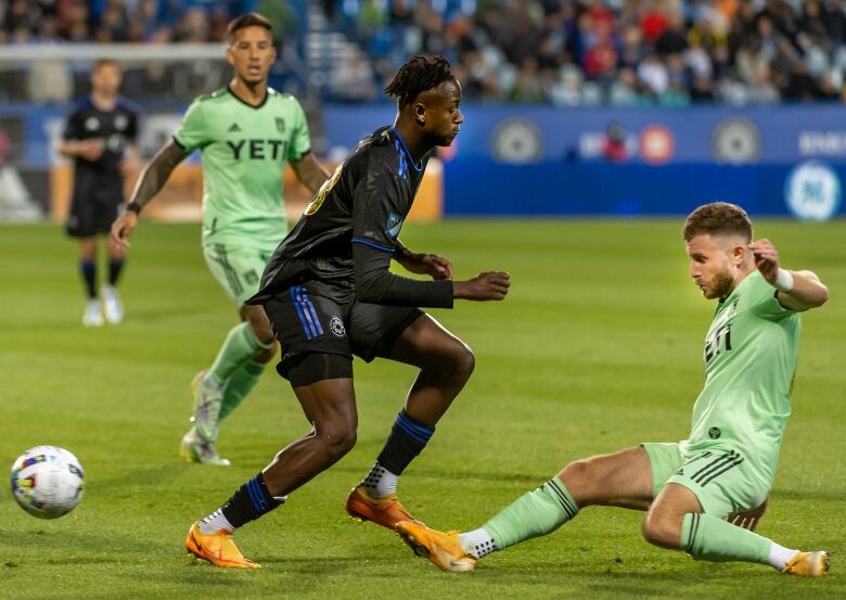 A soccer player in blue and black faces defence from two players in light green.