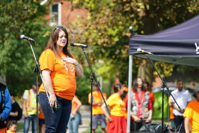 A woman with an orange shirt stands on stage.